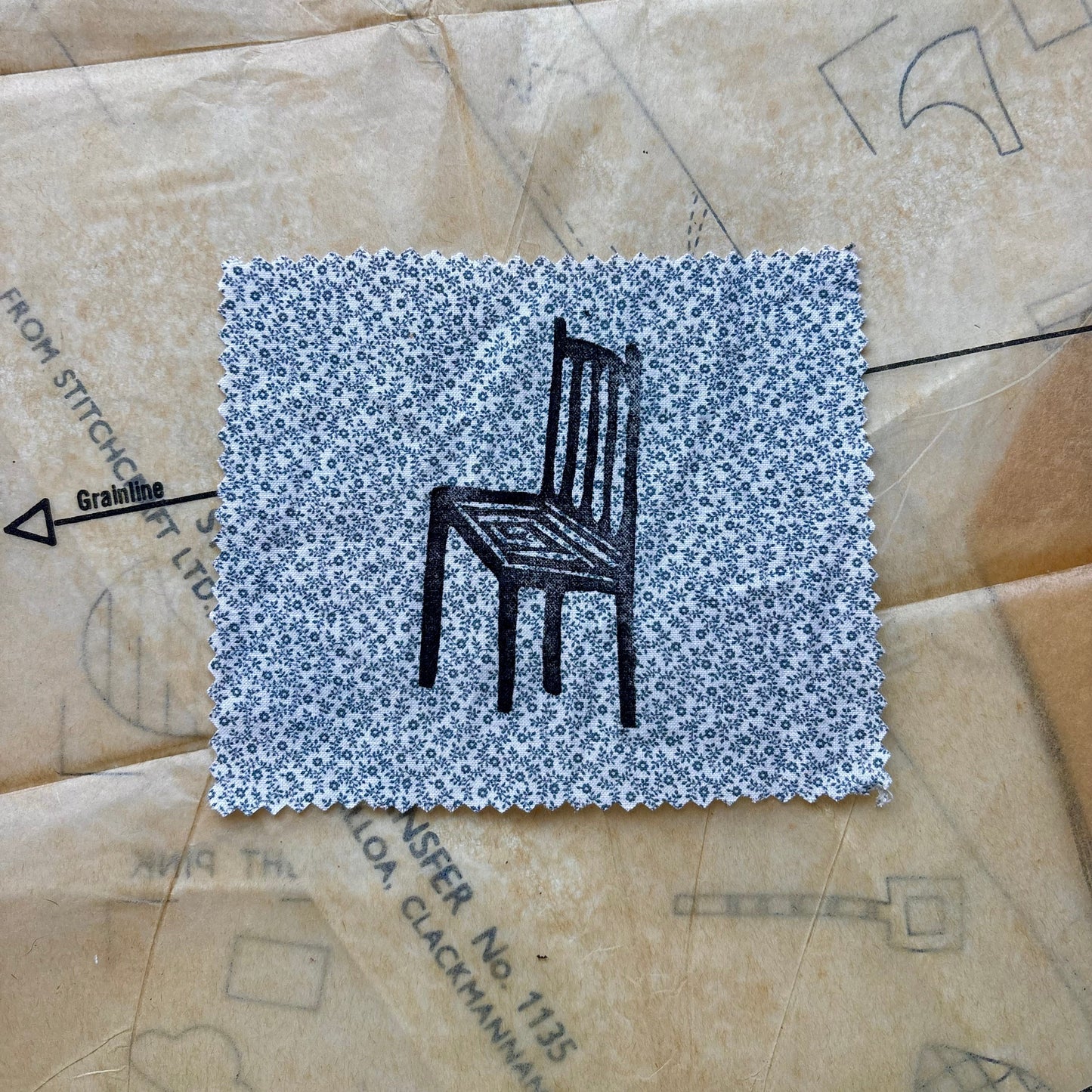 Small square of fabric with a black chair design on a textured surface