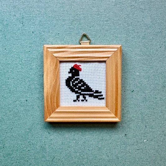 Small framed cross-stitched picture of a bird on a textured blue background