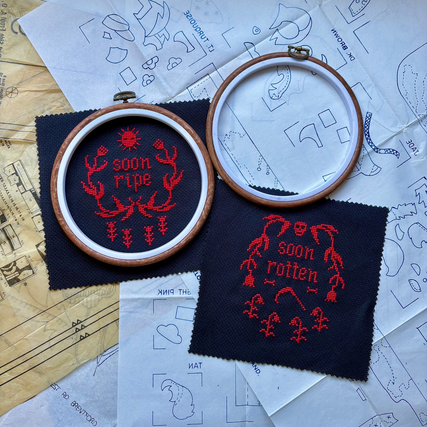 Embroidery hoops with red embroidered designs on black fabric, surrounded by patterned paper.