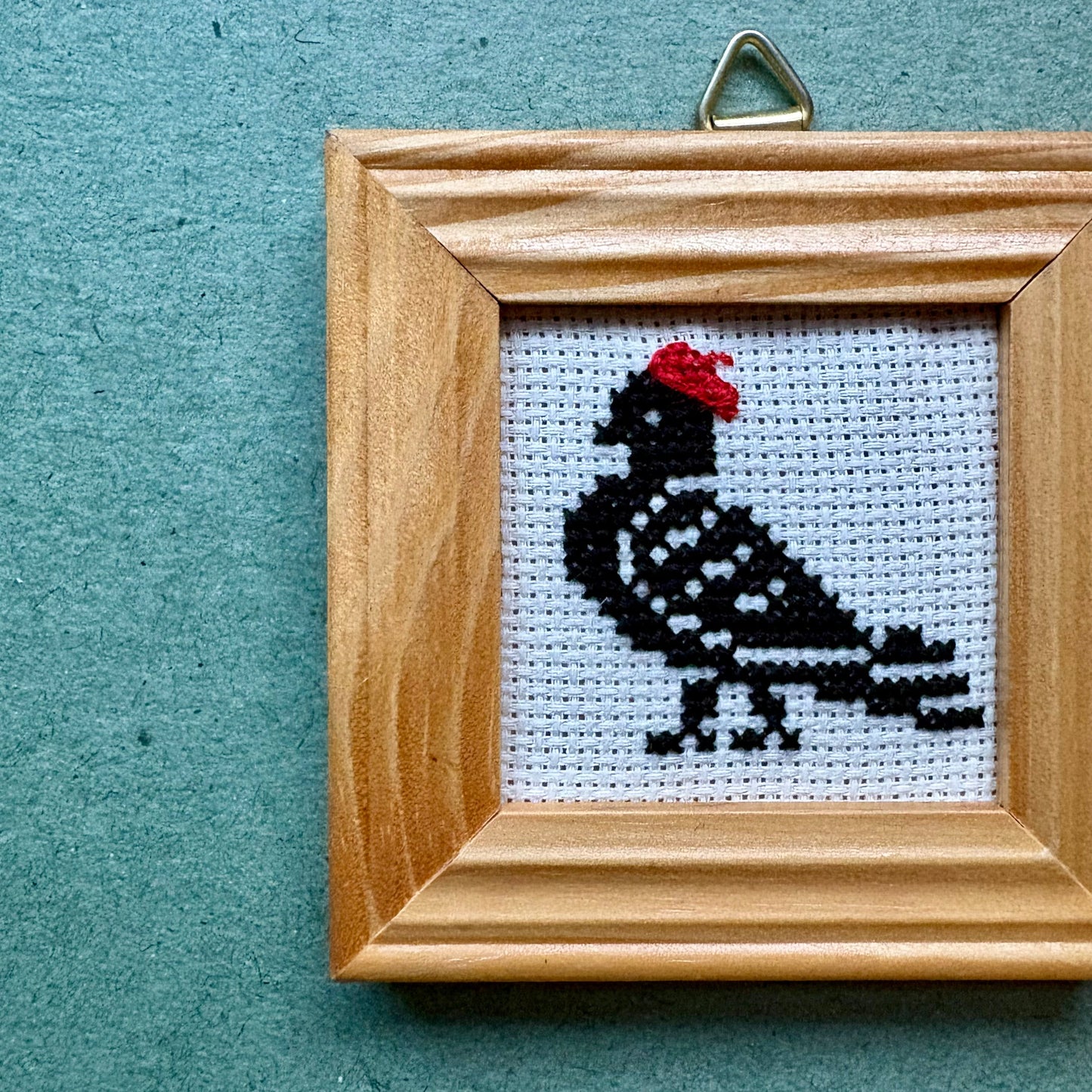 Wooden frame with a cross-stitched pigeon on a textured blue background