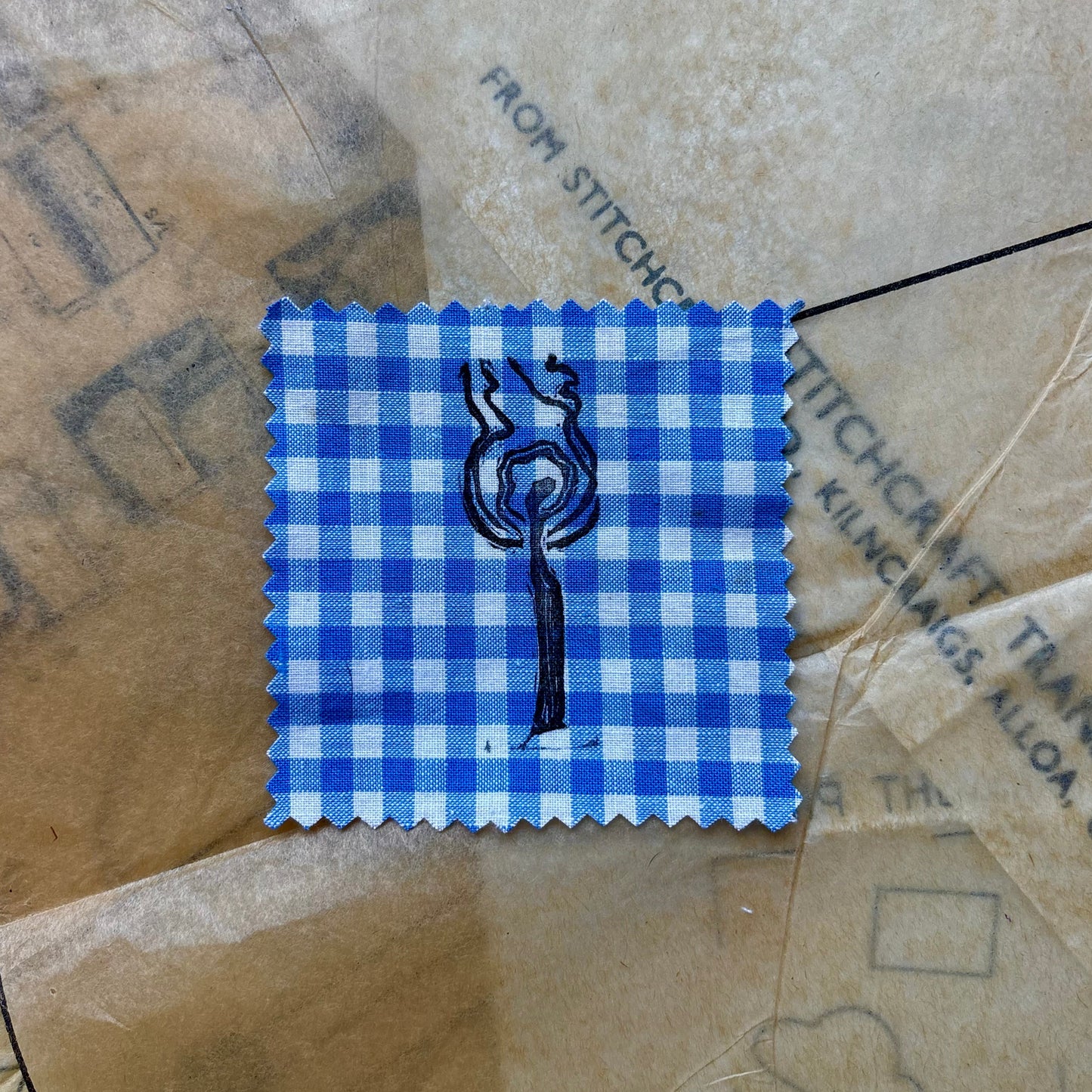 Blue checkered fabric swatch with a tree design on brown paper