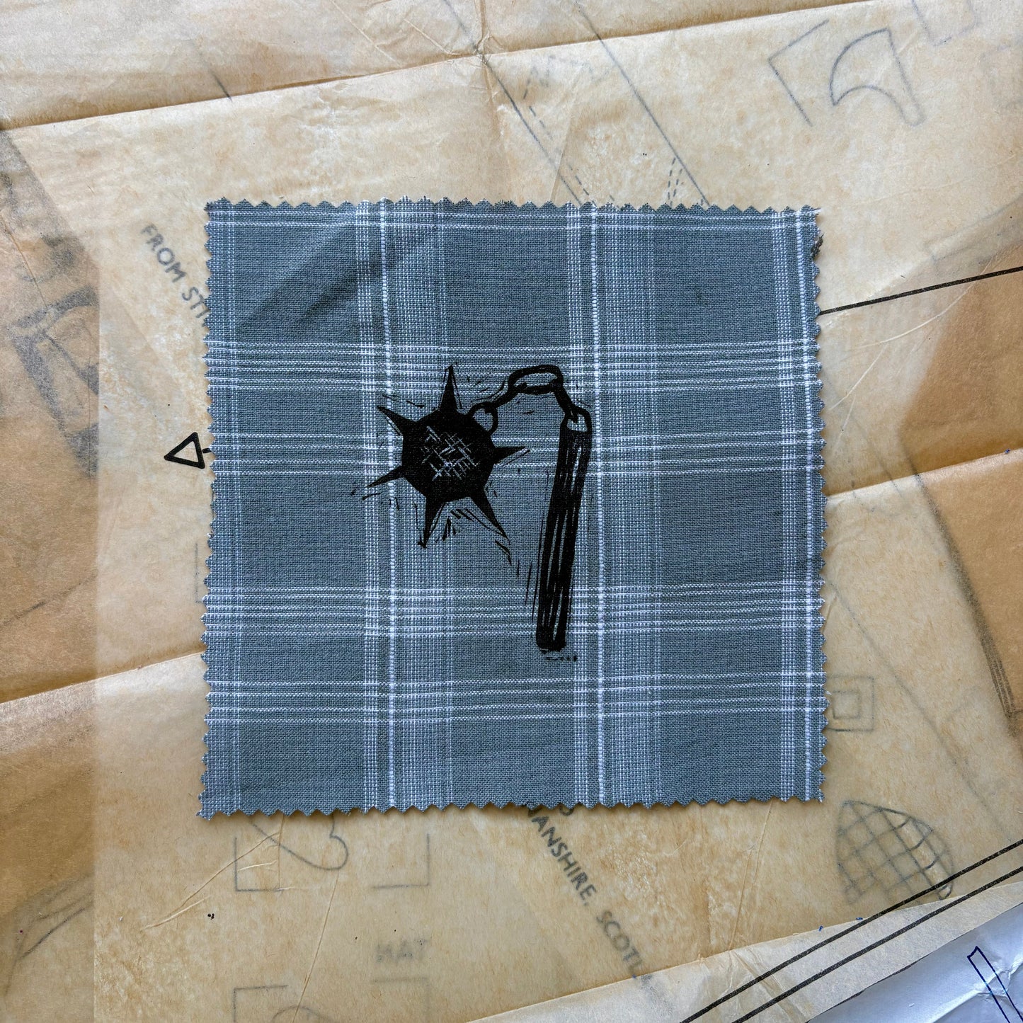 Blue plaid fabric swatch with black design on a textured beige surface