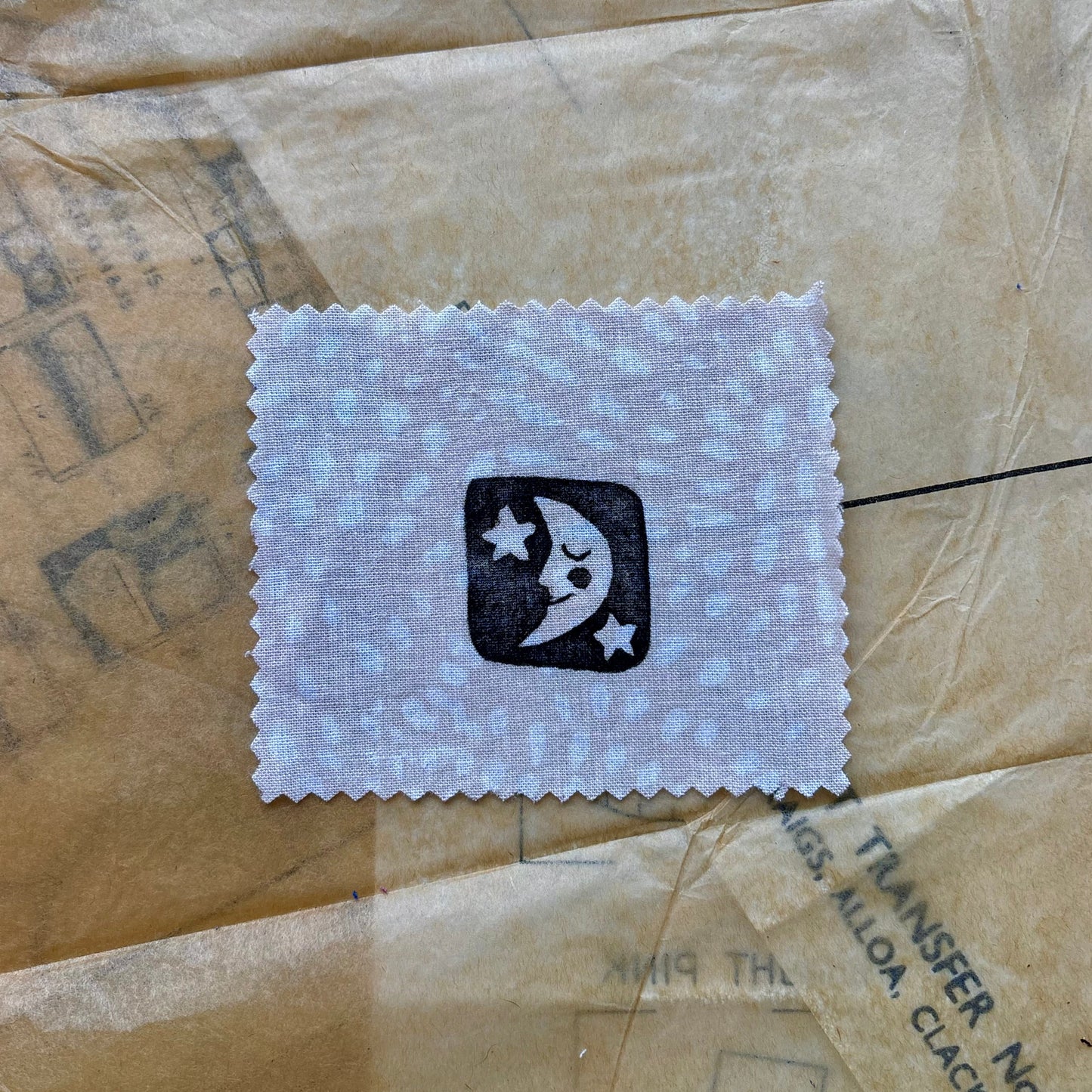 Small white cloth patch with a black logo on a textured brown surface