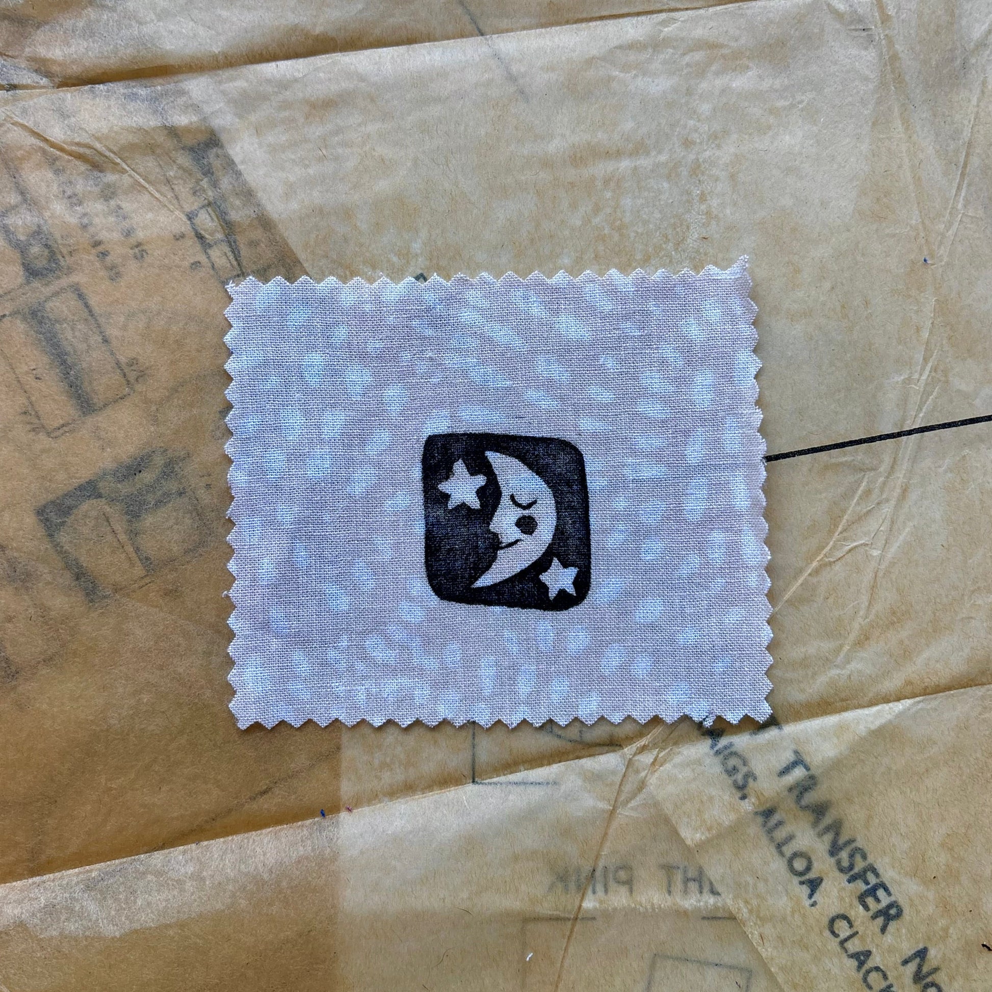 Small white cloth patch with a black logo on a textured brown surface