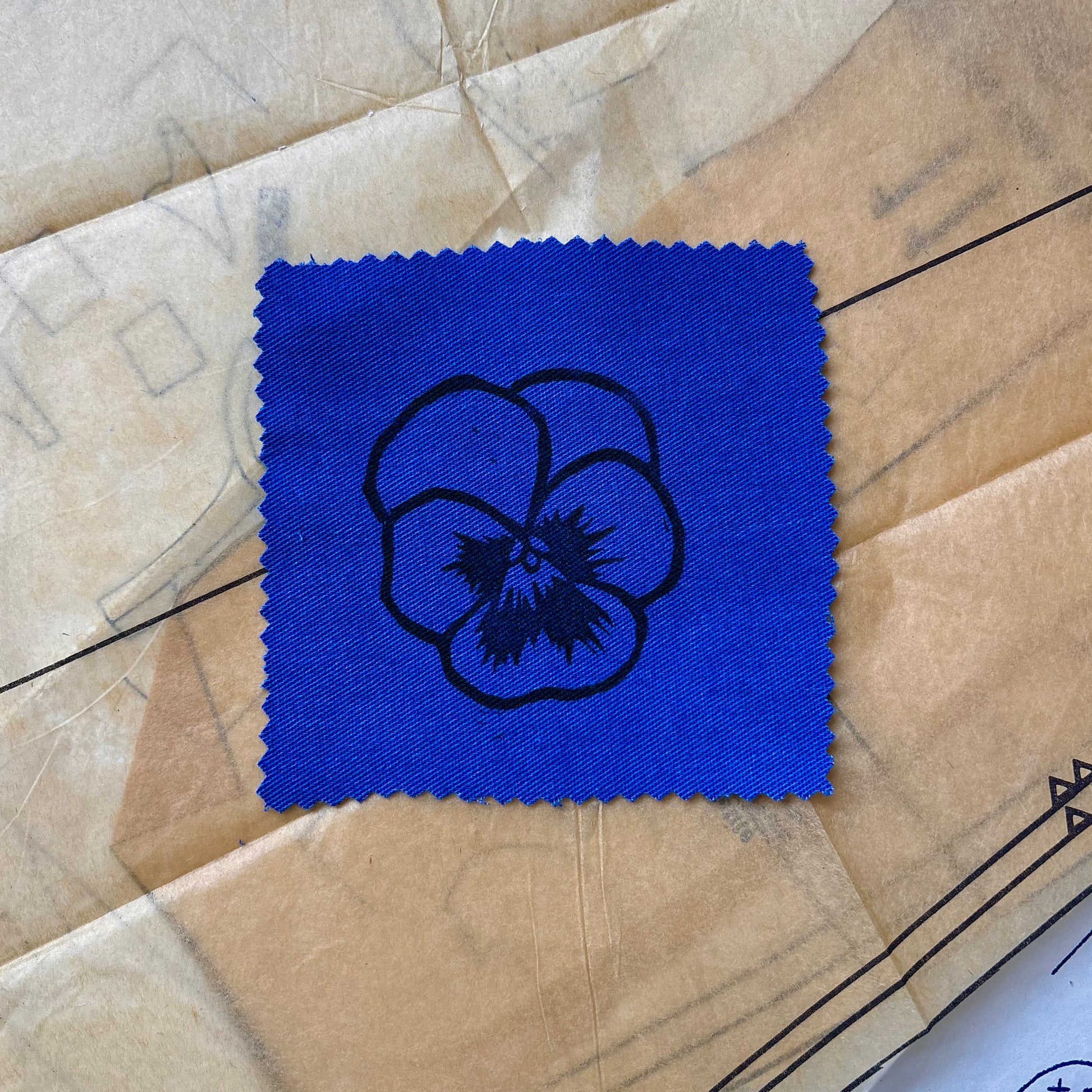 Blue square patch with a black floral design on a beige fabric background