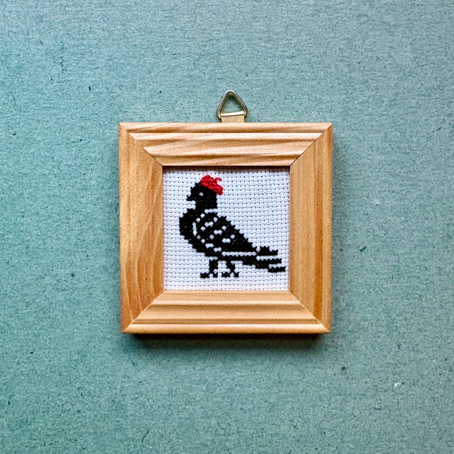 Small framed cross-stitched picture of a bird on a textured blue background