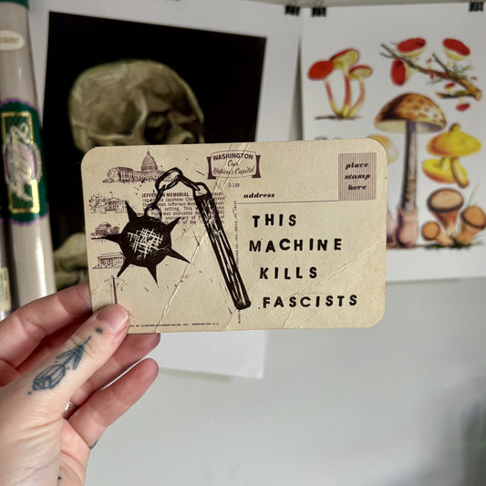 Hand holding a card with a graphic design and text, with a skull and mushroom poster in the background.