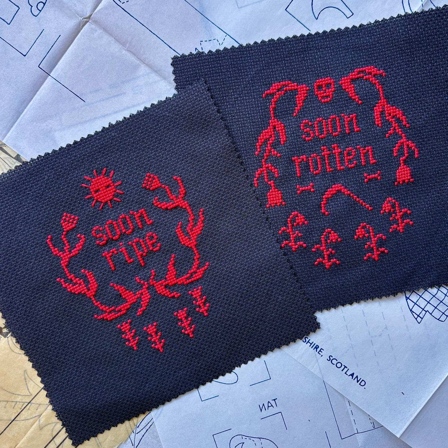 Two pieces of navy fabric with red embroidered designs on a surface with blue patterns.