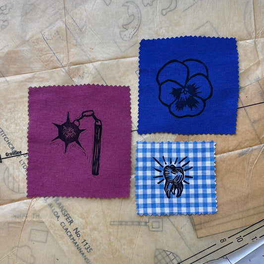 Three fabric swatches with printed designs on a textured surface with blueprints.