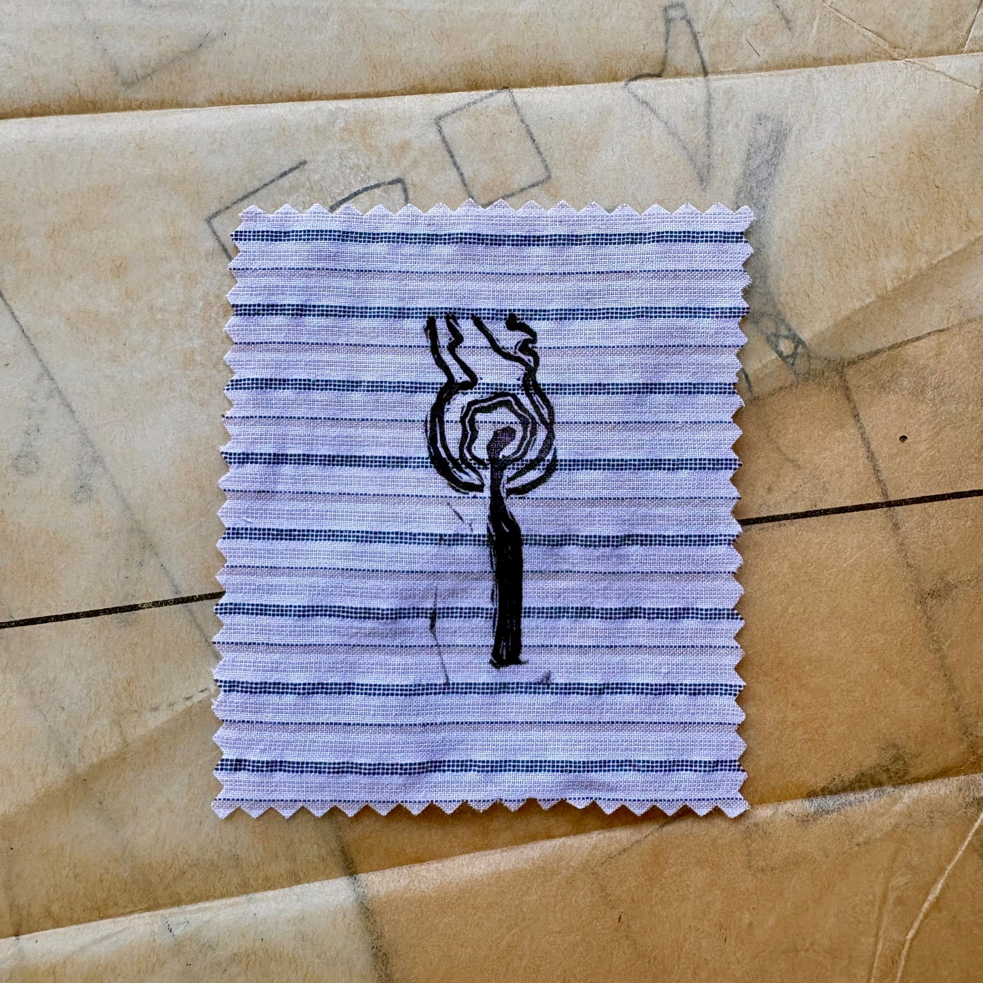 Square of striped fabric with a black tree drawing on a textured beige surface