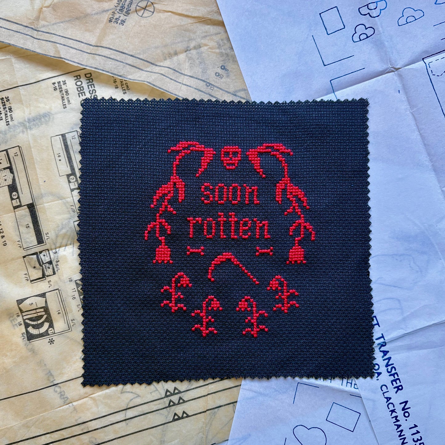 Cross-stitched patch with red design on black fabric, placed on patterned paper.