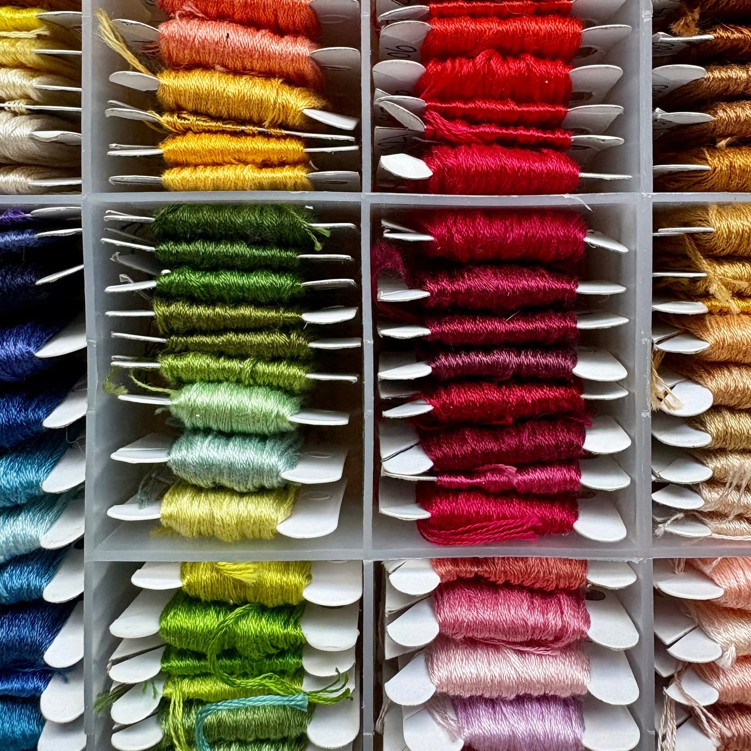 Colorful spools of embroidery thread arranged in a grid on a white background