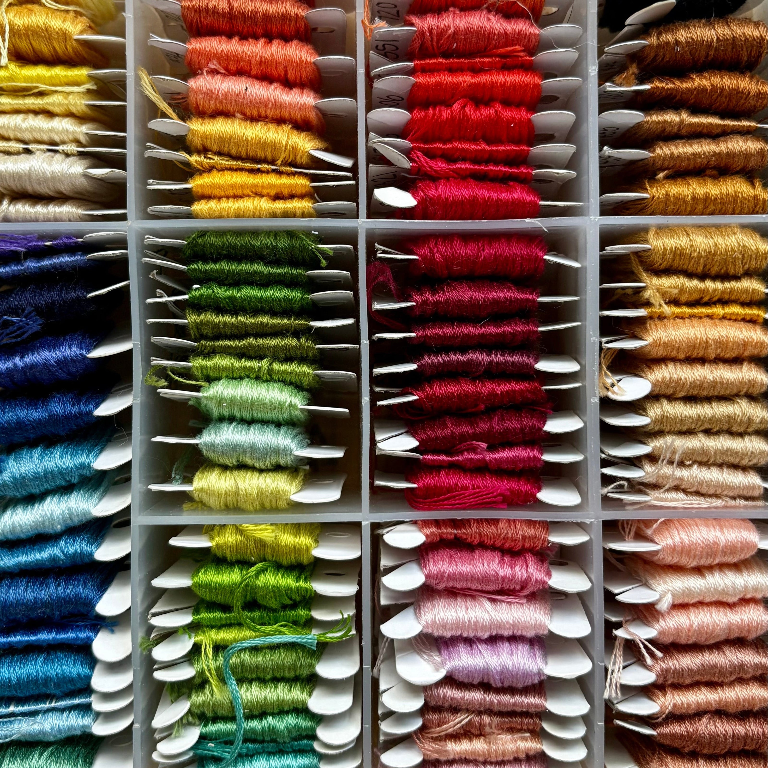 Assorted spools of thread in a clear plastic case on a wooden surface